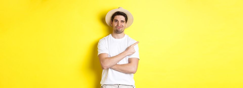 Concept of tourism and lifestyle. Skeptical guy tourist complaining, pointing finger left at something bad, looking displeased, yellow background.