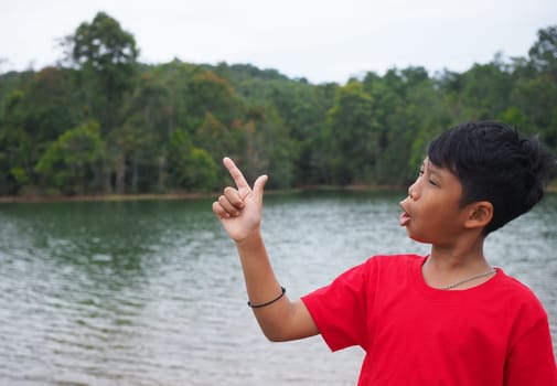The boy smiled and pointed his hand to his side. On the background is a reservoir.