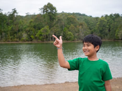 The boy smiled and pointed his hand to his side. On the background is a reservoir.