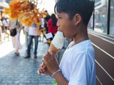 A boy wearing a white shirt is eating ice cream.