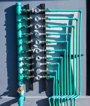 Water meter panels, water valves, and green water pipes arranged on the wall of the building