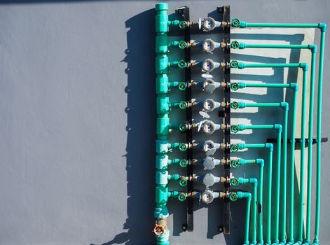 Water meter panels, water valves, and green water pipes arranged on the wall of the building