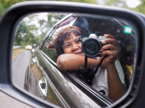 A woman holds a digital camera and takes a picture of herself smiling reflected in the car mirror.