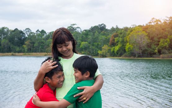 Happy family spending time outdoors hugging and enjoying the view of river. Mother with two kids.