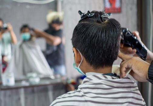 Teenage boy in a face protective mask is getting a haircut from a barbershop. Fashionable elongated haircuts for boys. Beauty salon in quarantine coronavirus covid-1