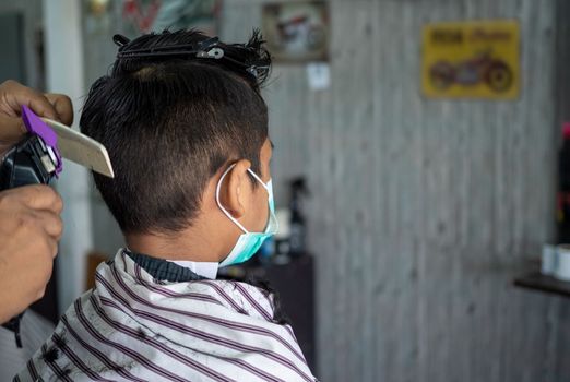 Teenage boy in a face protective mask is getting a haircut from a barbershop. Fashionable elongated haircuts for boys. Beauty salon in quarantine coronavirus covid-1