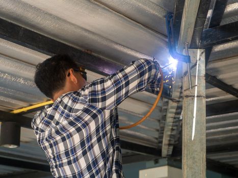 A welder is working on a steel frame. At the construction site.