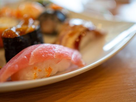 Various sushi in a white plate placed on a wooden table