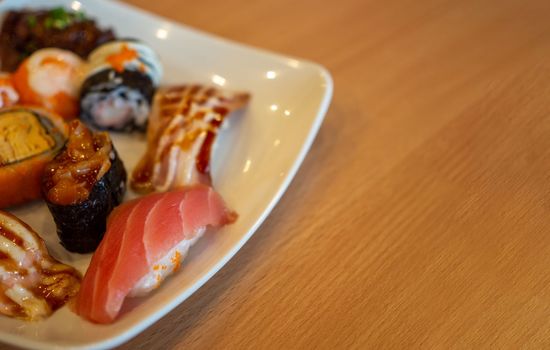 Various sushi in a white plate placed on a wooden table