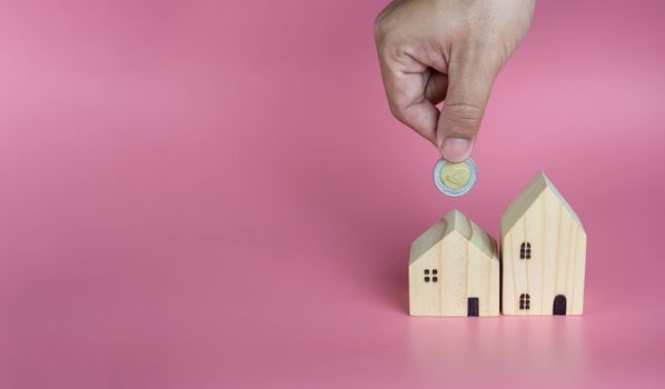 A human hand put a coin in the model house. Ideas for saving money to buy a new home and loans for planning future real estate investments.