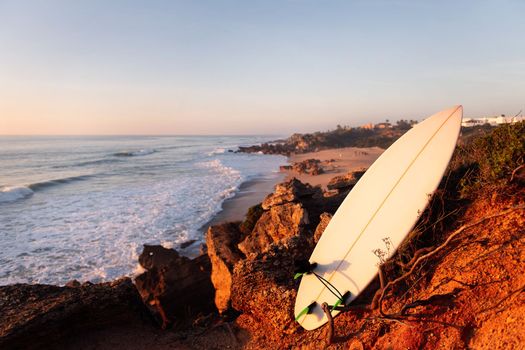 surfboard on the rocks of a cliff by the beach at sunset, leisure and hobbies concept, copy space for text