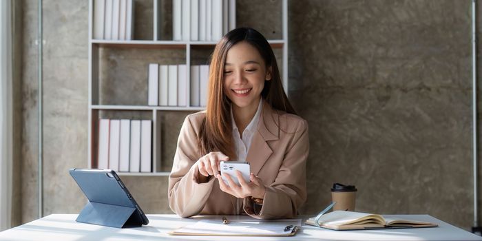 Smiling asian business woman with smartphone in office. Woman in suit at office.