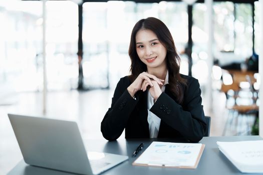 Portrait of a woman business owner showing a happy smiling face as he has successfully invested her business using computers and financial budget documents at work.