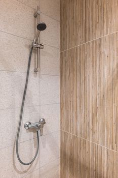 Closeup of a shower area with marble tiles on the walls and metall faucet with a long hose and a shower head
