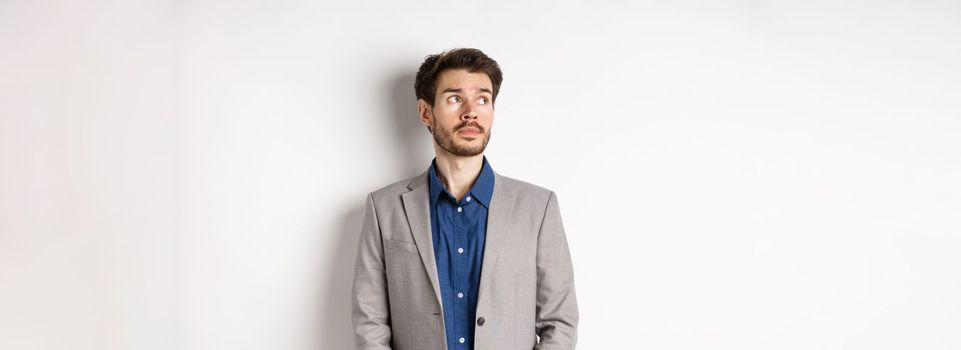 Thoughtful sad businessman in suit looking at upper left corner logo, thinking or spacing out, standing on white background.