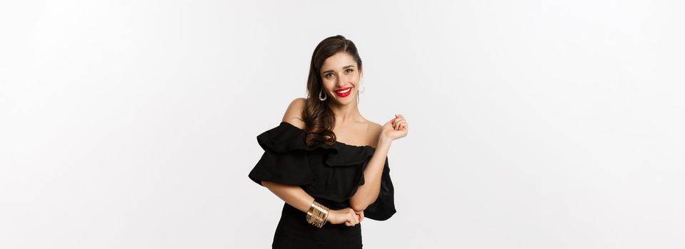 Fashion and beauty. Woman celebrating and dancing in black dress, having fun and smiling, standing over white background.