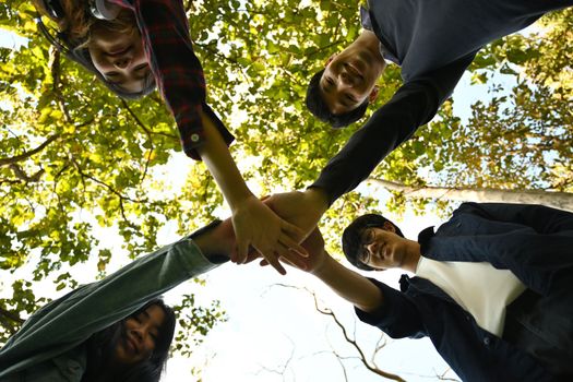 Low angle view of young people stacking hands together. University, youth lifestyle and friendship concept.