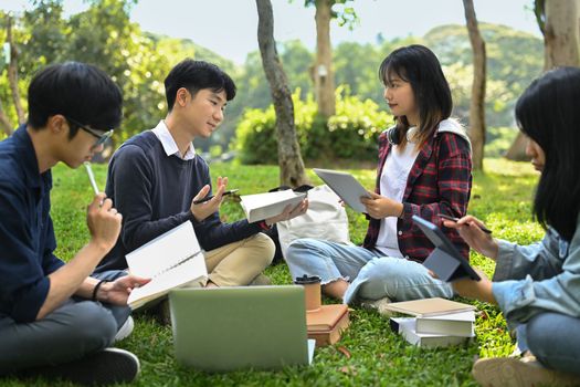 Group of happy young friends sitting in college campus and talking. University, youth lifestyle and friendship concept.