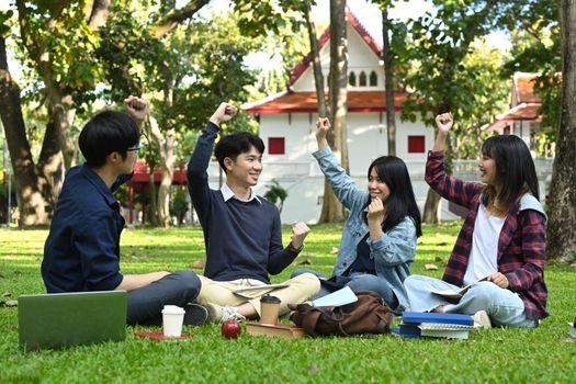 Excited university students with their hands raised, cheering successful exam pass together. Youth lifestyle and friendship concept.