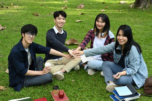 Group of university students stacking hands together and smiling to camera. University, youth lifestyle and friendship concept.