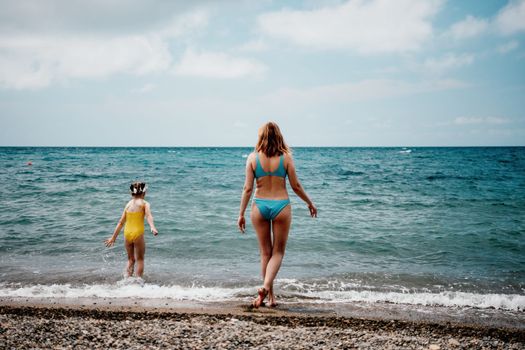 Happy loving family mother and daughter having fun together on the beach. Mum playing with her kid in holiday vacation next to the ocean - Family lifestyle and love concept.