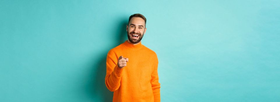 Handsome man laughing and pointing at camera, nodding in approval, agree with you, standing over light blue background.