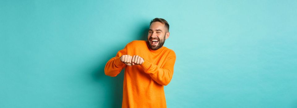 Happy man dancing and celebrating success, feeling like winner, smiling and rejoicing, light blue background.