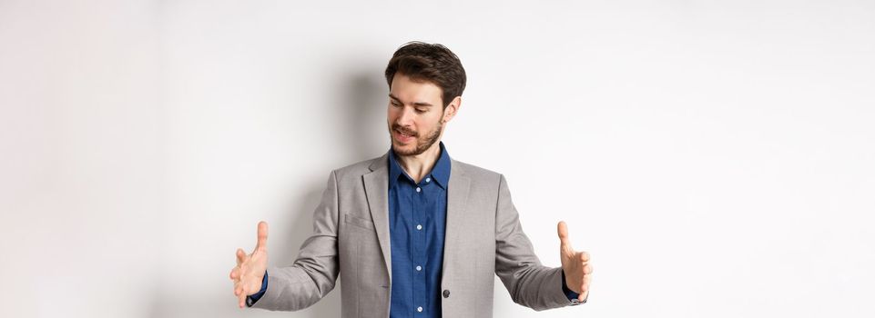 Excited handsome businessman showing long size thing, big object with stretch out hands, standing in suit on white background.