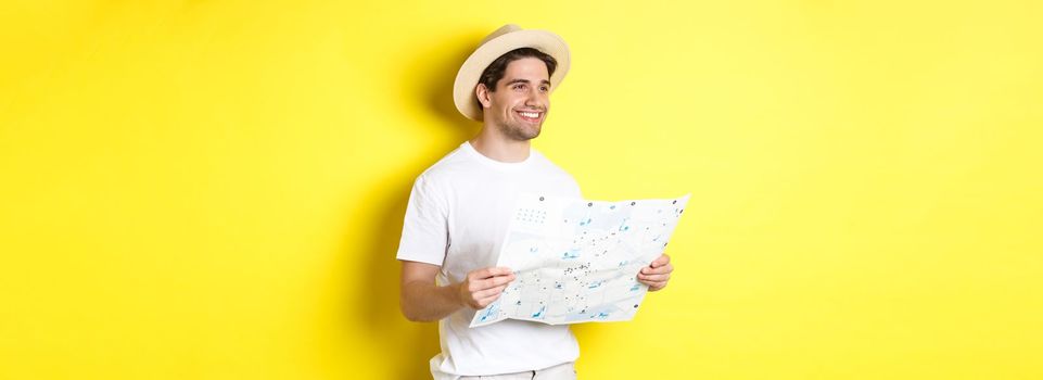 Travelling, vacation and tourism concept. Handsome guy tourist going sightseeing, holding map and smiling, standing over yellow background.