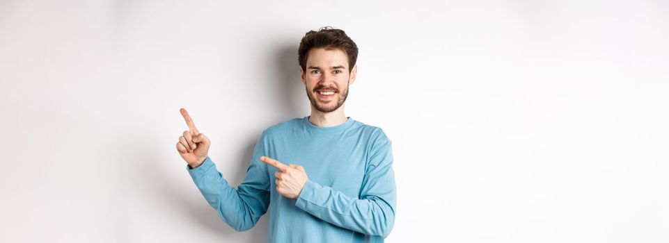 Happy bearded man showing advertisement, pointing fingers right and smiling, inviting to click link, standing over white background.