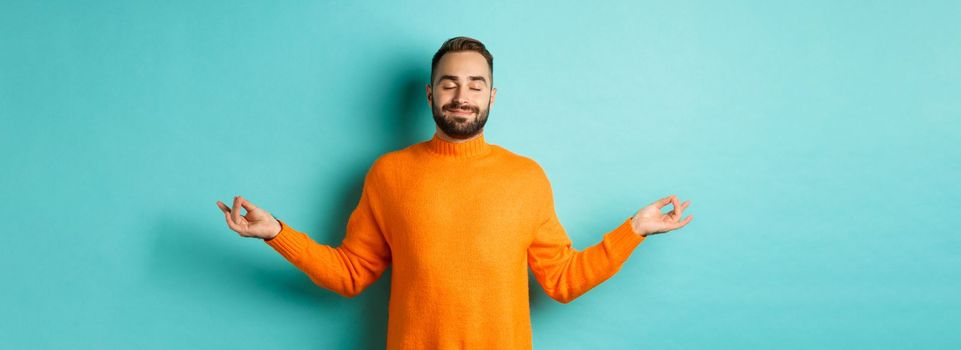 Image of relaxed and relieved man close eyes and smiling, feeling stress-free, meditating with calm expression, standing over light blue background.