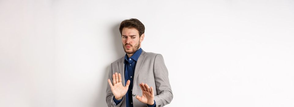 Stay away. Reluctant businessman step back with concerned disgusted face, raising hands to block bad offer, rejecting something awful, tilting from disgust, white background.