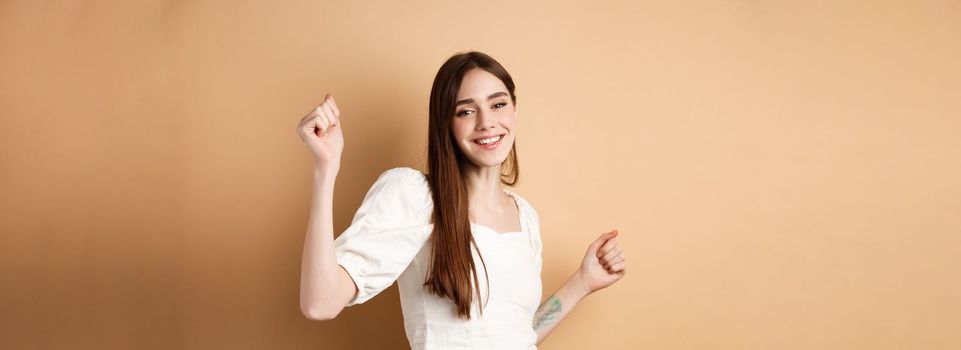 Happy woman dancing and having fun, close eyes and smiling, standing on beige background.