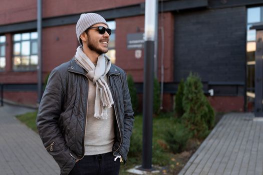stylish young man in sunglasses and hat with scarf outside.