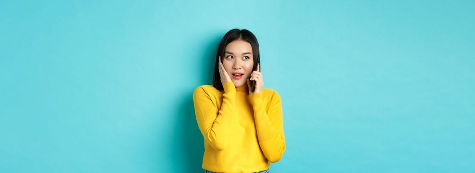 Woman looking intrigued while talking on mobile phone, receive interesting offer during call, standing over blue background.