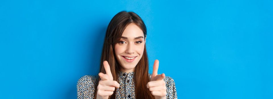 Excited and confident beauty woman, pointing fingers at camera and smiling, invite and beckon you, join us gesture, praising good choice, standing on blue background.