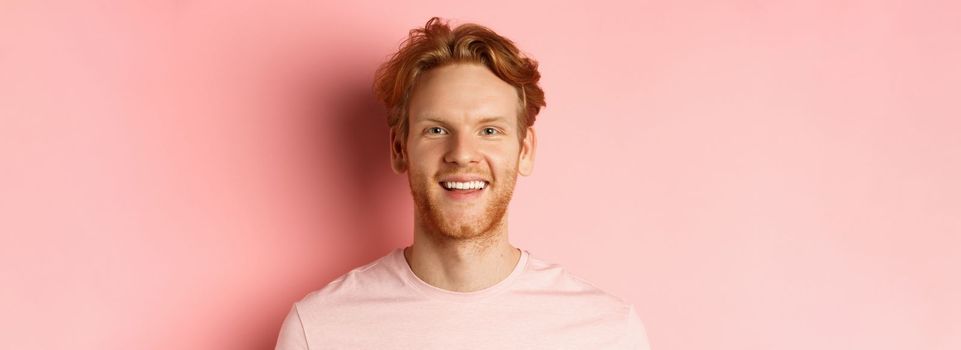 Headshot of happy redhead man with beard and white teeth, smiling excited at camera, standing over pink background.