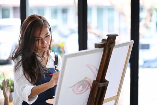 Attractive woman painting picture on canvas at her creative workplace.