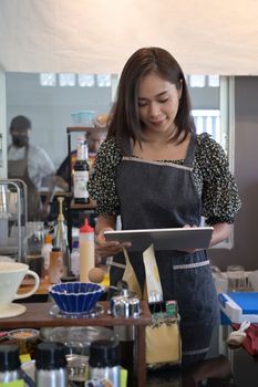 Portrait beautiful female barista using digital tablet while standing at counter in coffee shop.