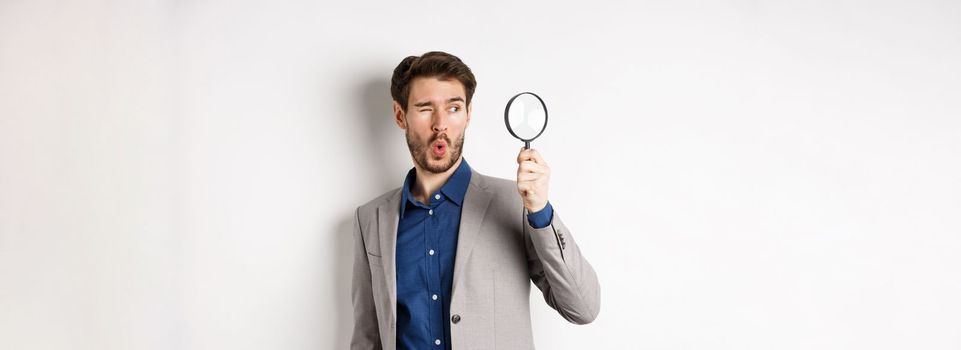 Excited funny guy in suit look through magnifying glass aside, checking out awesome thing, found something, white background.