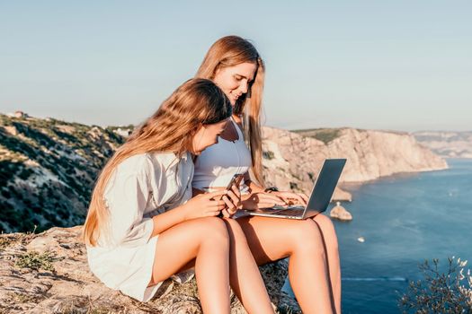 Successful business woman in yellow hat working on laptop by the sea. Pretty lady typing on computer at summer day outdoors. Freelance, travel and holidays concept.