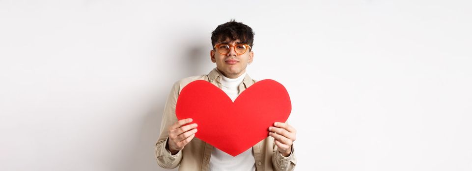 Passionate man waiting for lover with big red heart on Valentines day, looking romantic and with love, standing over white background.