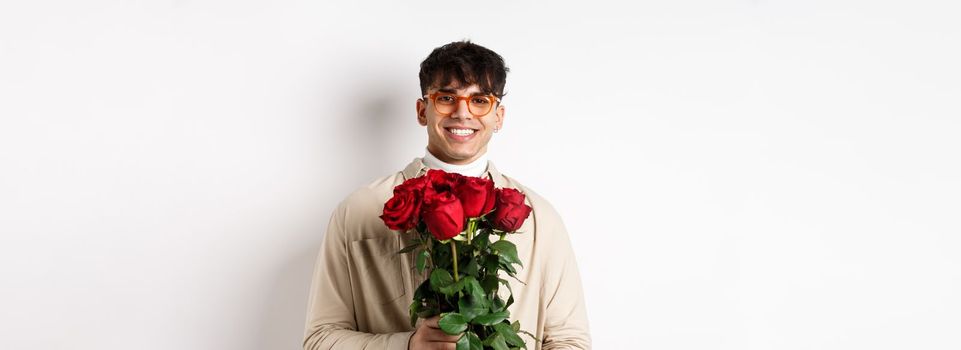 Handsome hipster guy waiting for his lover with bouquet of roses. Young man with flowers standing on Valentines day over white background.