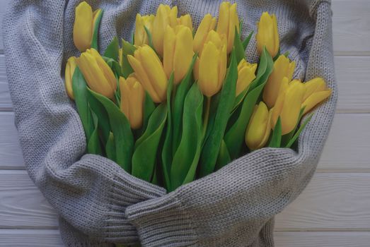 A bouquet of yellow tulips is located in a gray women's sweater