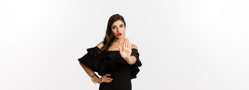 Fashion and beauty. Confident attractive woman telling no, showing stop gesture and looking serious at camera, disapprove and prohibit, standing over white background.