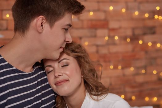 Relation emotions. Young man embracing attractive brunette wife indoor. They are in love and happy