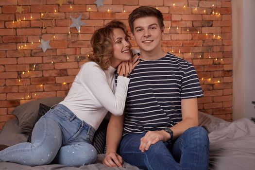 Happy loving couple relaxing on bed at home, young woman touching smiling handsome man face, looking in the eyes. enjoying togetherness and tenderness in love, close up view