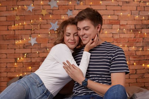Happy loving couple relaxing on bed at home, young woman touching smiling handsome man face, looking in the eyes. enjoying togetherness and tenderness in love, close up view