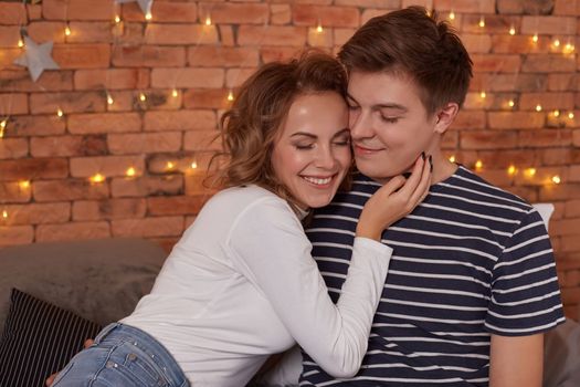 Happy loving couple relaxing on bed at home, young woman touching smiling handsome man face, togetherness and tenderness in love, close up view