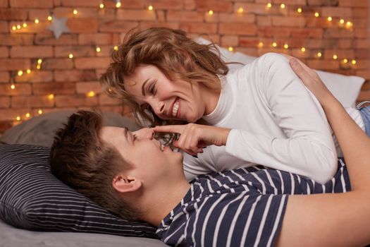 Caucasian young beautiful couple lie on bed and hugging each other. They look each other in the eyes and they are happy